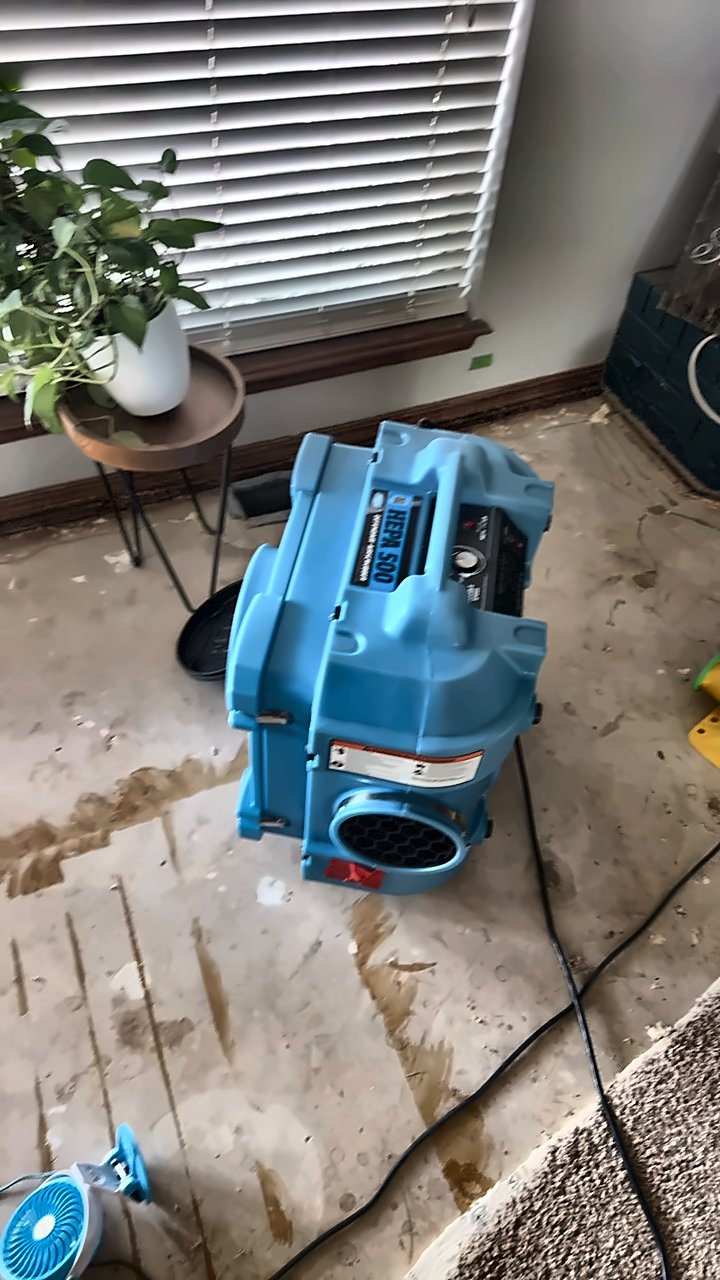 A HEPA air scrubber runs on a stripped, stained subfloor during a 4D Restoration dry-out.