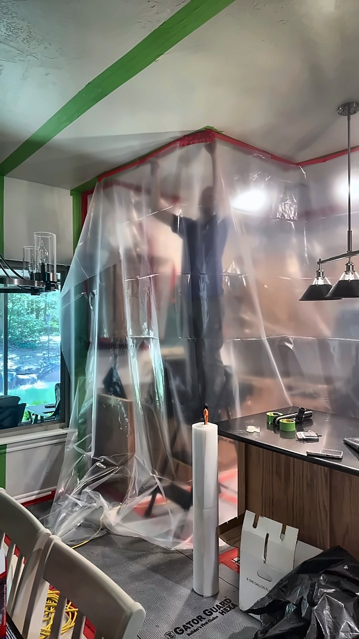 A 4D Restoration crew member hangs clear plastic sheeting to build a containment wall in a kitchen.
