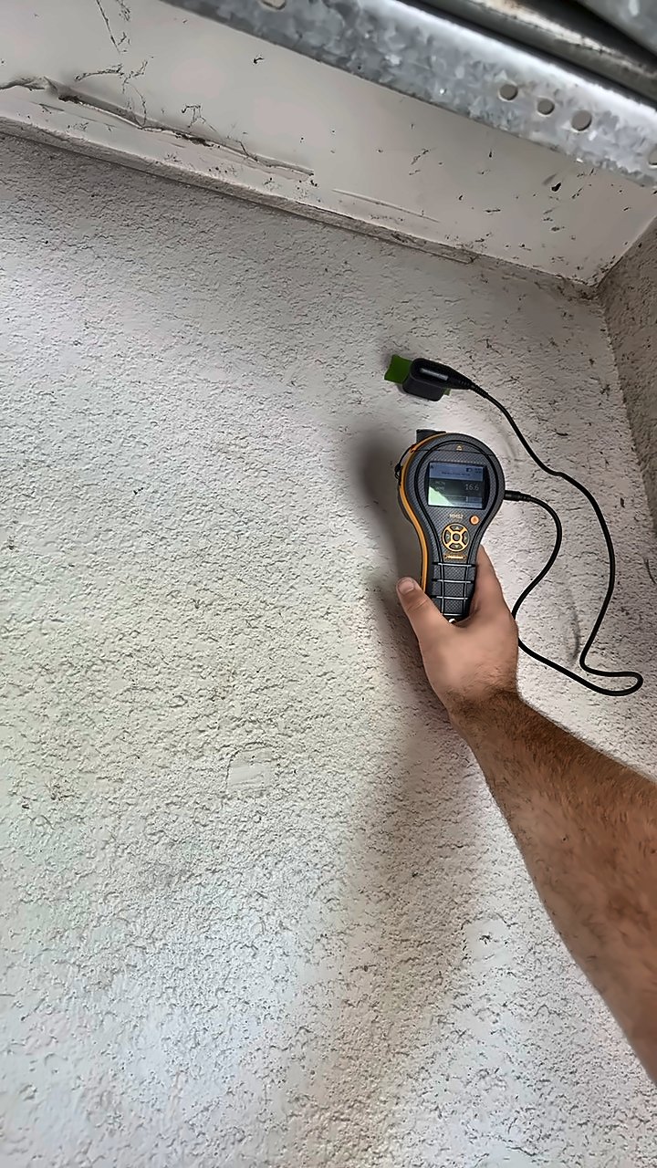 A 4D Restoration tech holds a moisture meter against a wall near the ceiling, reading through a taped-on sensor.