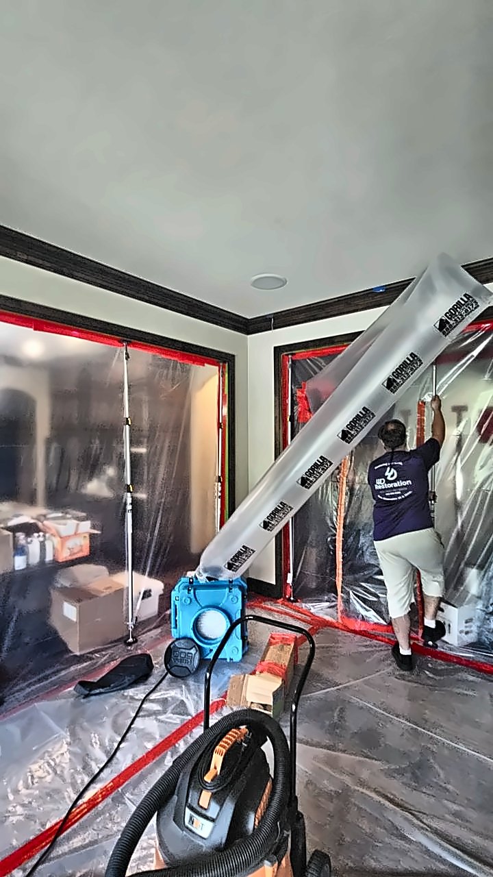 A 4D Restoration tech works inside taped plastic containment with an air scrubber ducting air out of the zone.