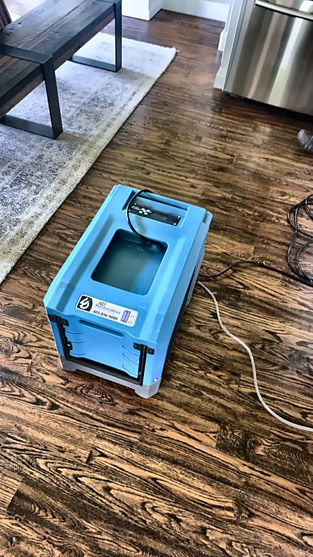 A 4D Restoration industrial dehumidifier, the company logo and phone number visible on its side, runs on a hardwood floor during a dry-out.