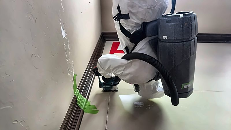 A 4D Restoration tech wearing a backpack HEPA vacuum works a wall seam beside a taped-off doorway.