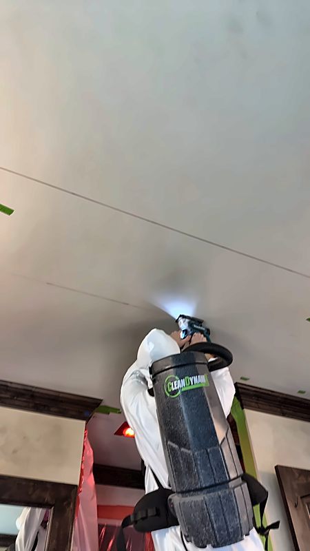 A hooded 4D Restoration tech works overhead with a lighted tool and backpack vacuum inside taped containment.