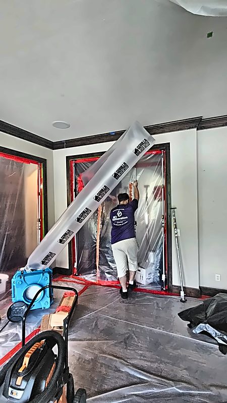 A 4D Restoration tech installs plastic containment around a doorway while an air scrubber runs.
