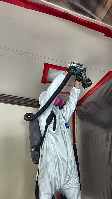 A suited 4D Restoration tech cuts ceiling material with a vacuum-captured multi-tool inside containment.